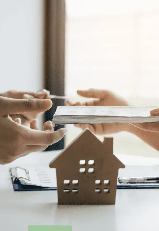 A contract being passed across a desk beside a model house
